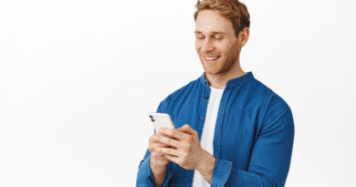 Modern Candid Guy With Phone Hands Chatting Message Read Screen Smiling Smartphone Display While Using Application Standing White Wall