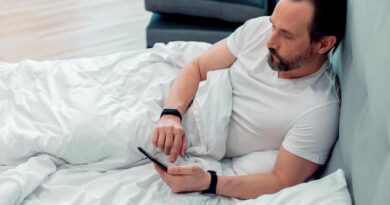 serious-bearded-man-white-tshirt-lying-pillow-bed-touching-screen-modern-smartphone