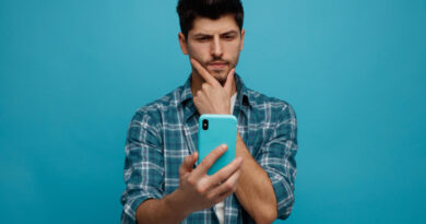 Suspicious Young Man Keeping Hand Chin Stretching Mobile Phone Out Towards Camera Looking It Isolated Blue Background