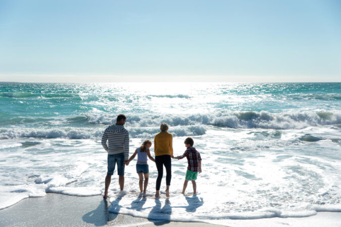 rear-view-caucasian-family-beach-with-blue-sky-sea-background-walking-water-holding-hands