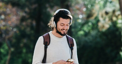 smiling-young-man-using-phone-listening-music-headphone-park