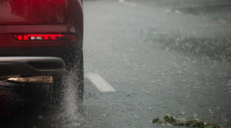 Rain Water Splash Flow From Wheels Red Car Moving Fast Daylight City With Selective Focus