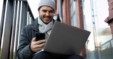 Young Man With Smile Looks Screen Laptop With Phone His Hands Outside