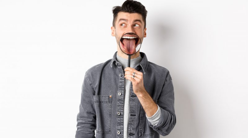 Handsome Positive Guy Showing White Perfect Teeth Tongue With Magnifying Glass Looking Left Logo Standing Against White Background