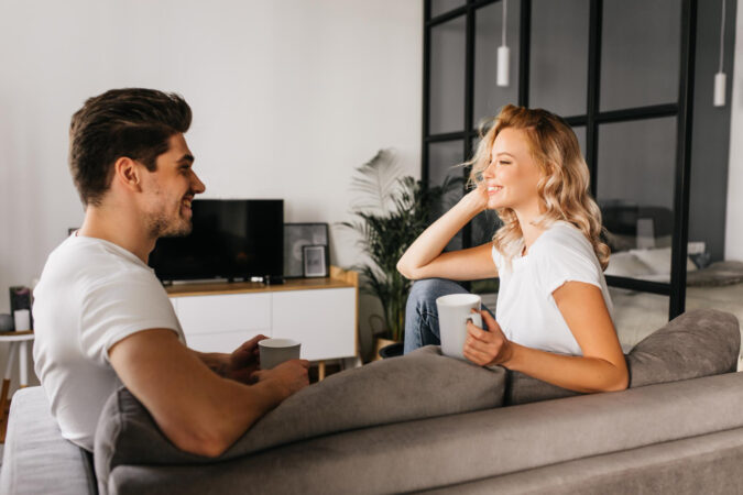 Smiling Young Couple Sitting Home Looking Each Other Holding Cups Cozy Home Photo Two Attractive People Love Spending Time Together