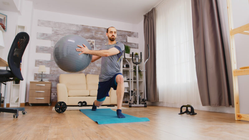 Athletic Guy Training Legs Using Swiss Ball Home Yoga Mat Living Room