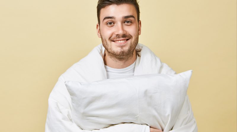 Positive Cheerful Young Man With Cute Smile Unshaven Face Standing Blank Wall Wrapped White Blanket Feeling Overjoyed Recovering From Cold Holding Pillow Going Sleep Bed