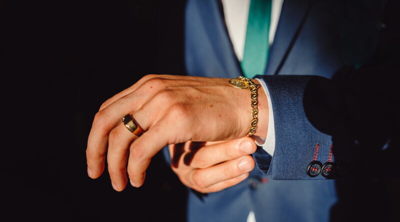 A Man Clasps A Gold Bracelet On His Arm. Hands Of Successful Businessman In Tuxedo, Closeup. Men's Accessories, Bracelet And Gold Ring On A Man's Hand.