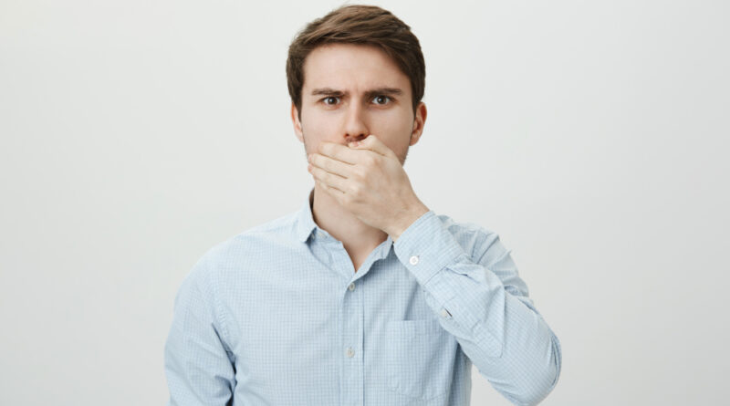 Shocked upset brunette man shut mouth with hand