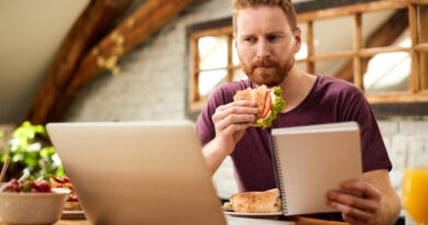 Mid Adult Man Eating Sandwich While Using Laptop Dining Table