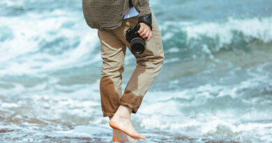 man-holding-professional-came-hand-walking-by-sea-rocky-beach