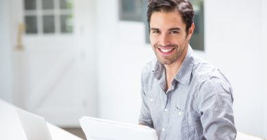 Smiling Young Man Holding Documents While Sitting Desk With Laptop