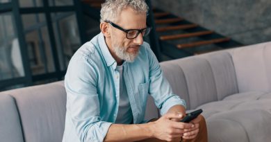 Senior Man Casual Clothing Eyeglasses Using Smart Phone While Sitting Sofa Home